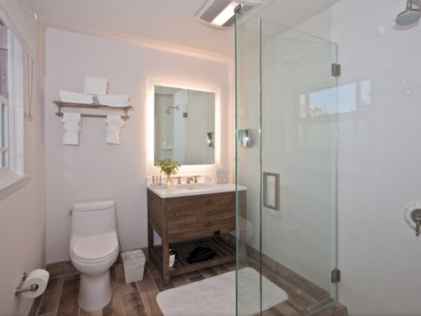 A modern bathroom features a glass-enclosed shower, a wooden vanity with a mirror, a toilet, and various decor items, including a small plant and toiletries.