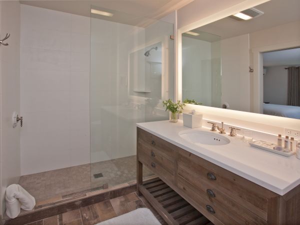 A modern bathroom features a glass-enclosed shower, a wooden vanity with a white countertop, a large mirror, and minimalistic decor.
