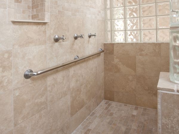 The image shows a spacious shower area with beige tiles, a built-in niche, multiple shower heads, a grab bar, and a glass block partition.