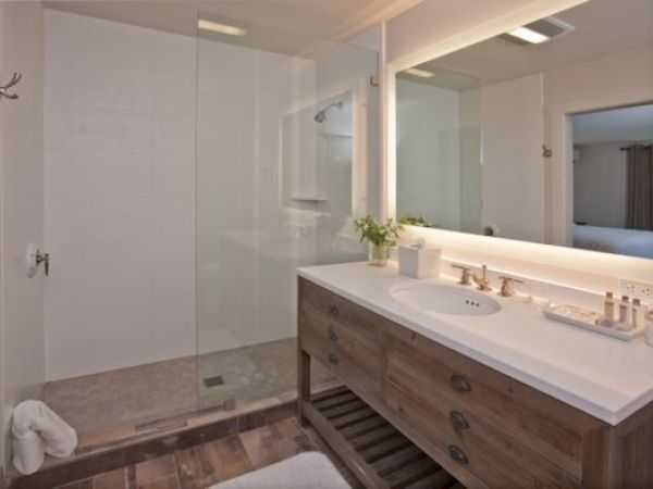A modern bathroom with a glass walk-in shower, wooden vanity with a large mirror, a sink, and bathroom essentials on the countertop ends the sentence.