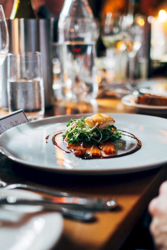 A dining table with plates of gourmet food, glasses of wine, and bread. People are seated and enjoying a meal, creating a cozy atmosphere.